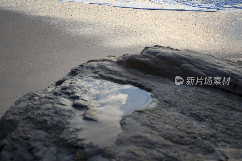 天空和云朵倒映在海滩的水坑里