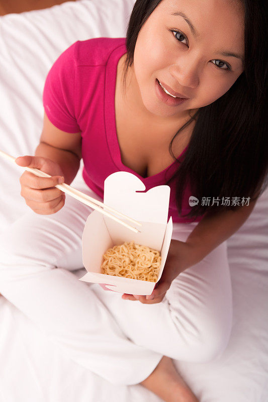 年轻的亚洲女性在床上吃中餐