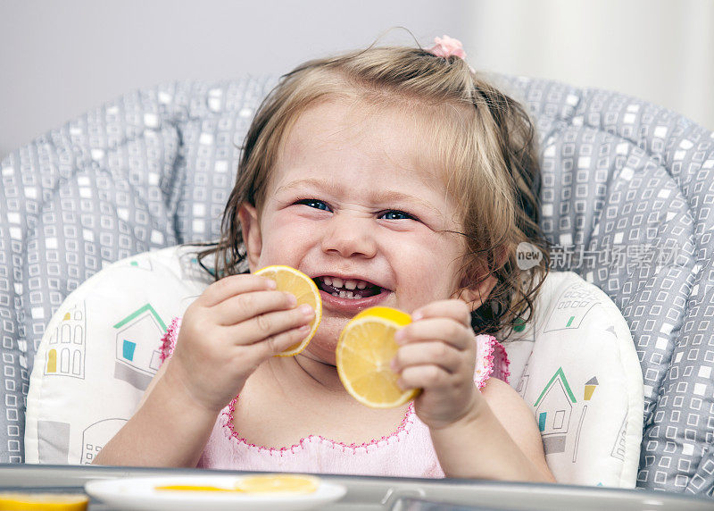 快乐的小女孩在高椅子上吃柠檬。