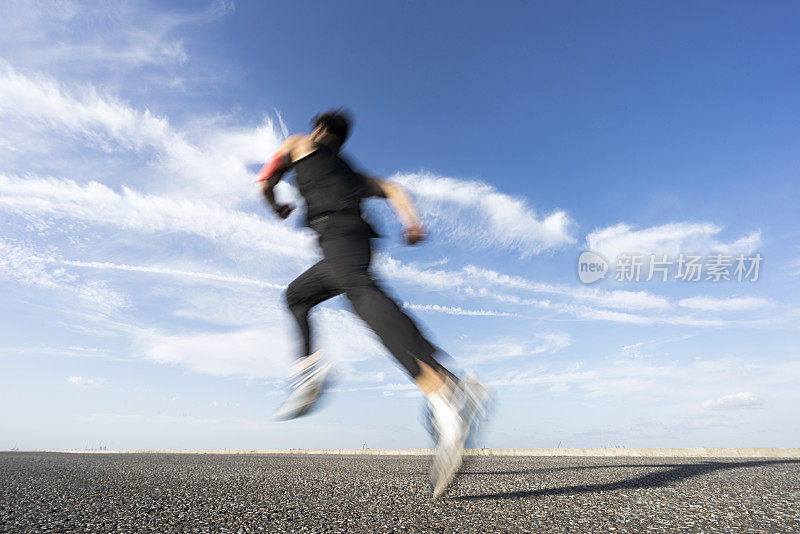 年轻的男运动员在柏油路上迎着天空奔跑