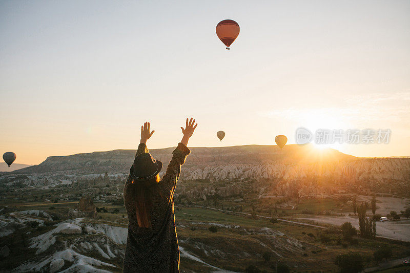 土耳其卡帕多西亚上空，一名戴着帽子的女游客正在欣赏热气球。令人印象深刻的景象。