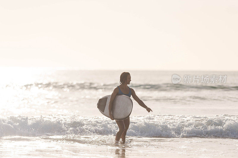 一名欧亚女性在冲浪一下午后背着她的冲浪板回来