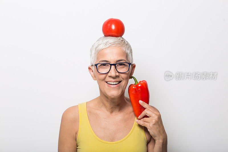 满脸笑容的老妇人，头上顶着番茄，手里拿着红辣椒