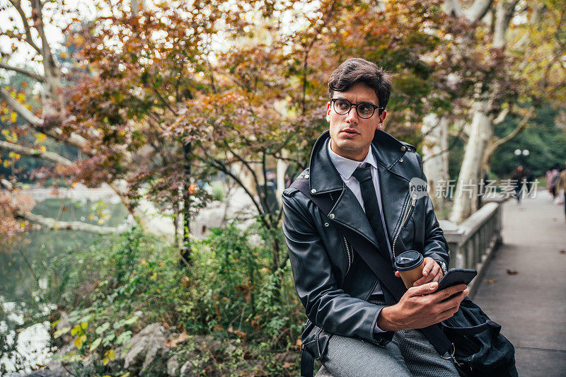一个男人坐在公园里，发短信，喝咖啡