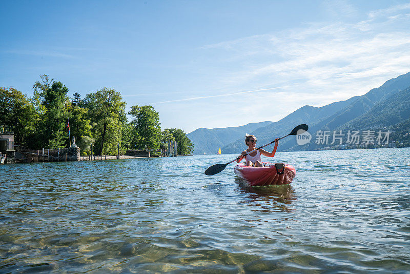 年轻女子在山湖上划着红色的独木舟