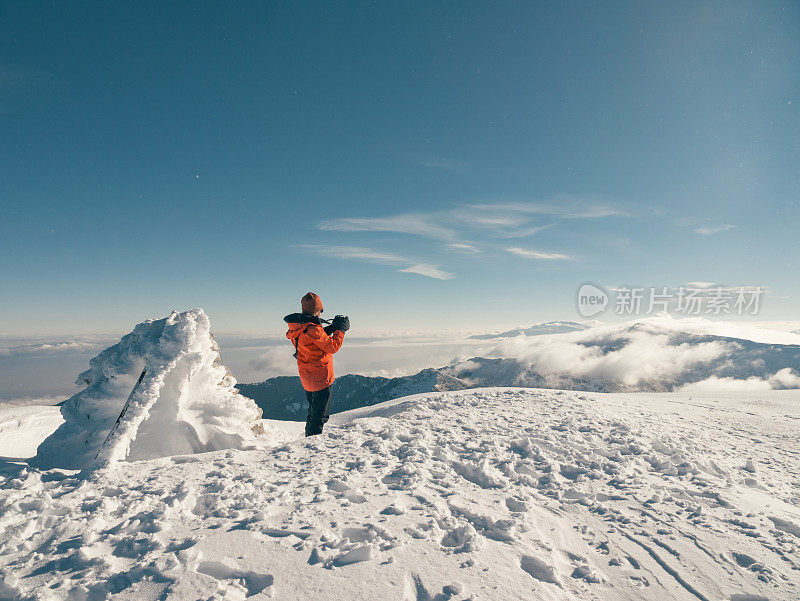 冬季日出时，女性高山攀登者在高海拔的山峰上拍照