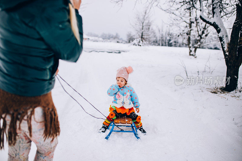 母亲和蹒跚学步的女儿在雪地里玩雪橇