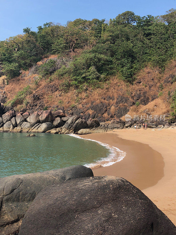 热带岛屿天堂的图像，蝴蝶海滩，Palolem，果阿，印度，棕榈树，私人附近的蜜月海滩与金色的沙子，温暖的绿松石海背景照片，岩石，悬崖面和游客度假