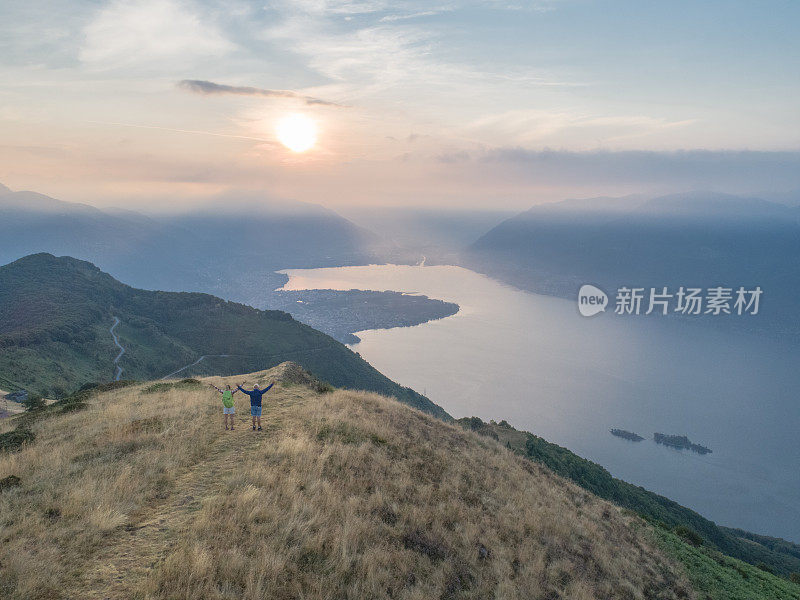 无人机航拍父亲和女儿在清晨徒步登山，拥抱大自然的清新，张开双臂等待成功