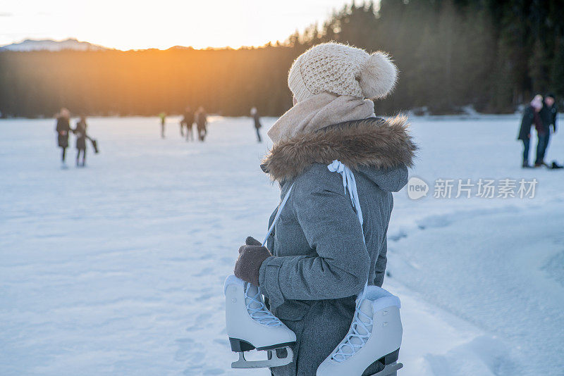 夕阳西下，年轻女子肩挎冰鞋走在结冰的湖面上，享受着寒假的乐趣