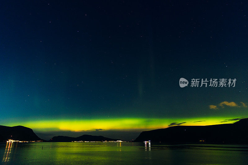 风景秀丽的北极光在峡湾和发光的城镇在挪威