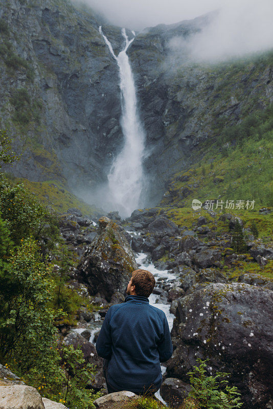 一个男人旅行者考虑在挪威瀑布风景山谷的后视图