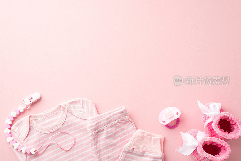 婴儿配件概念。顶部视图照片的粉红色婴儿衣服衬衫裤子假牙链和针织靴子孤立的粉彩粉红色背景与空白