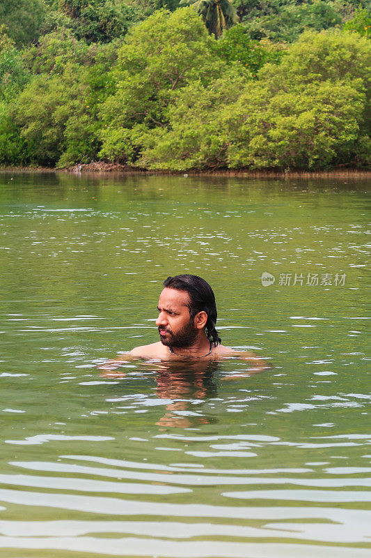 一个印度人在泻湖平静的海水中游泳和戏水的特写照片，热带岛屿天堂，林地和棕榈树的景色，重点在前景