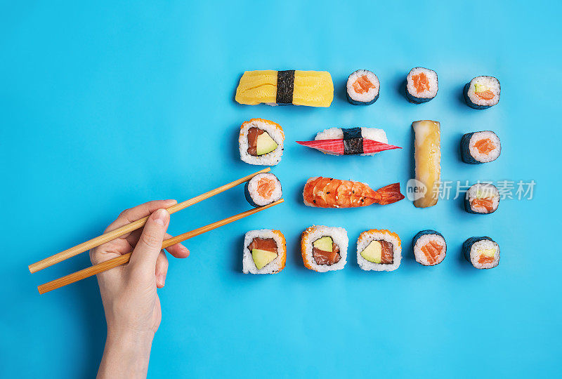 吃寿司的女人。蓝色背景上的各种寿司卷和寿司团。