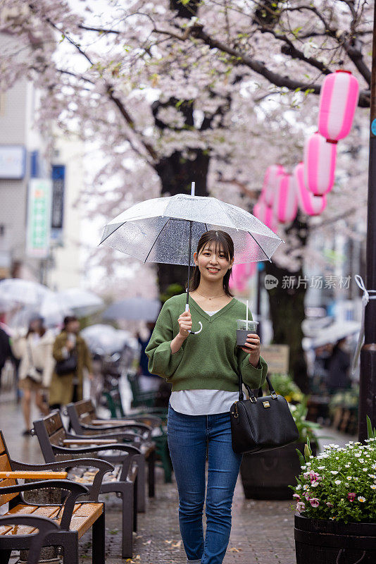 年轻女子走在樱花下在城市在一个雨天-看着相机