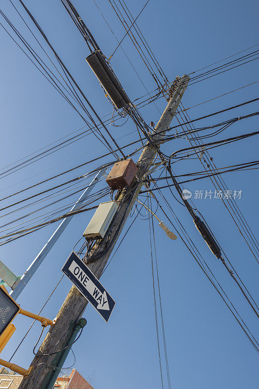 一根木制电线杆上杂乱的互联网和电视电缆、电话线和电线映衬着蓝天。