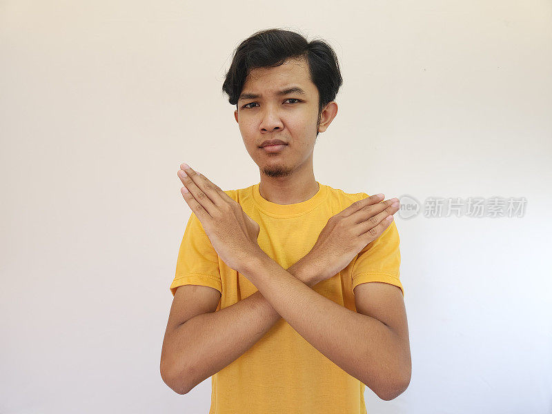 年轻英俊的亚洲男子的肖像，表现出停止或拒绝的表情，双臂交叉做否定的手势，愤怒的脸，孤立的蓝色背景