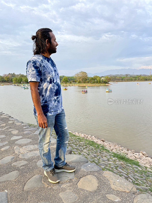印度人在昌迪加尔苏赫纳湖岸的特写照片，他看着水库水面上的船只、独木舟、脚踏船和皮划艇，候鸟保护区，国家湿地