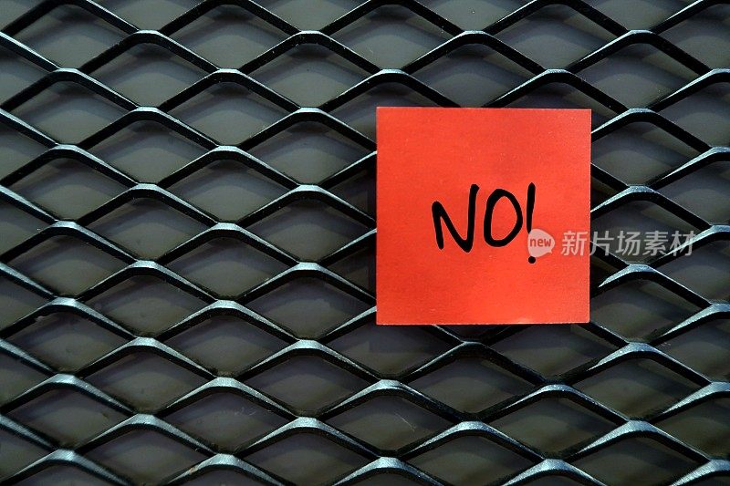 一个红色的便签纸贴在深色的背景上，上面写着NO!提醒自己敢于拒绝或无所畏惧地说不的概念