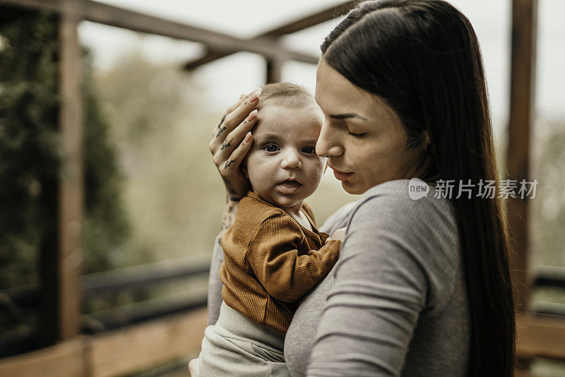 美丽的年轻妈妈站在后院，怀里抱着她可爱的小男孩或小女孩。