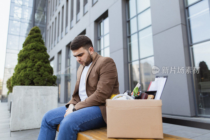 面对失业:一个男人坐在长凳上，带着私人物品，感觉很沮丧