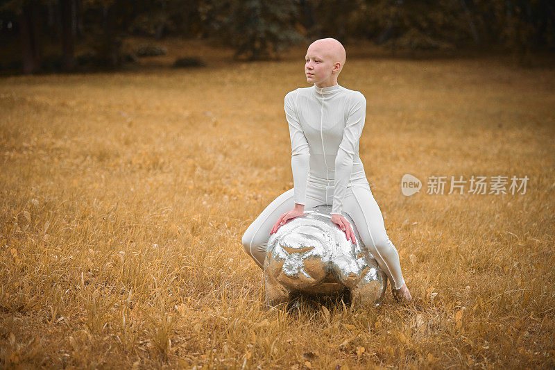 在秋天的公园里，穿着白布、秃顶的年轻无毛女孩坐在缓步动物的雕像上