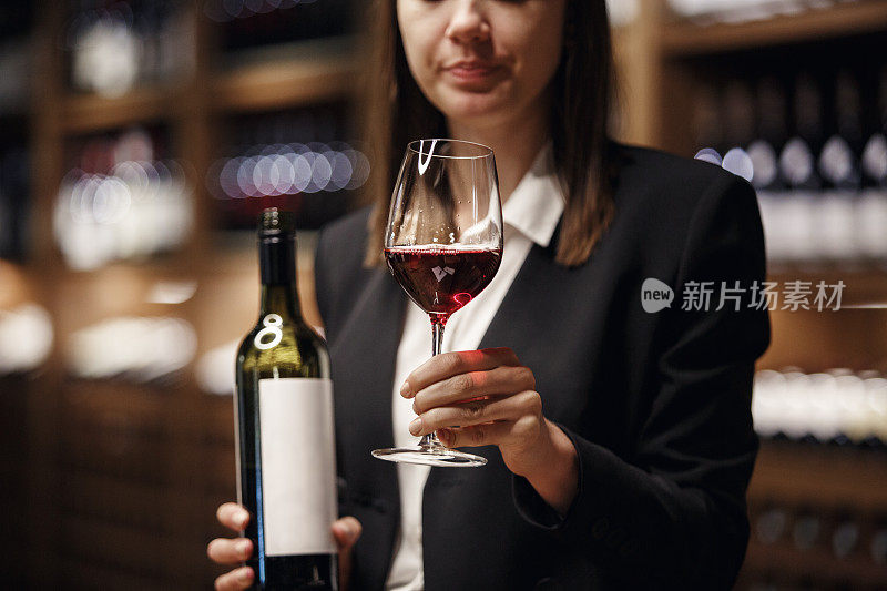 专业的餐厅工作人员拿着开瓶和满杯的红酒杯站在酒窖背景上。