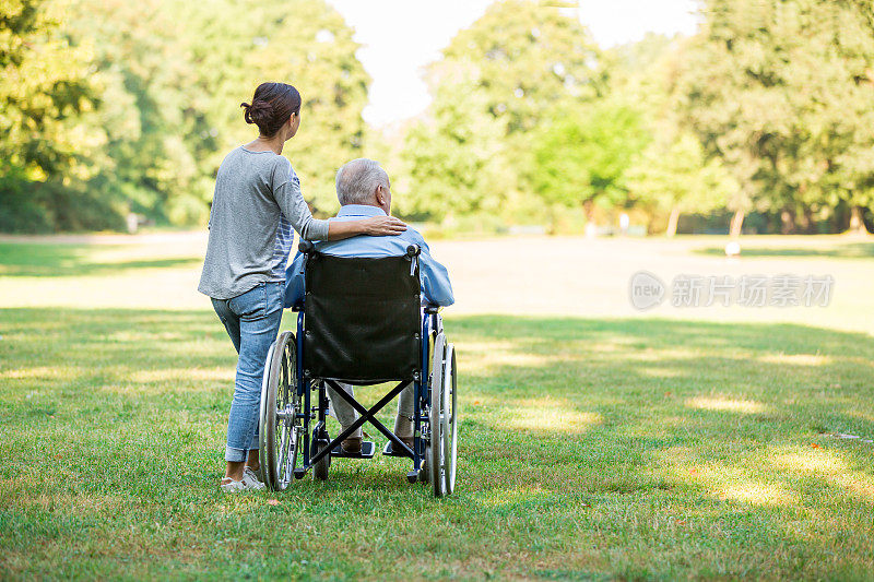 护理人员和坐在轮椅上在户外行走的老人