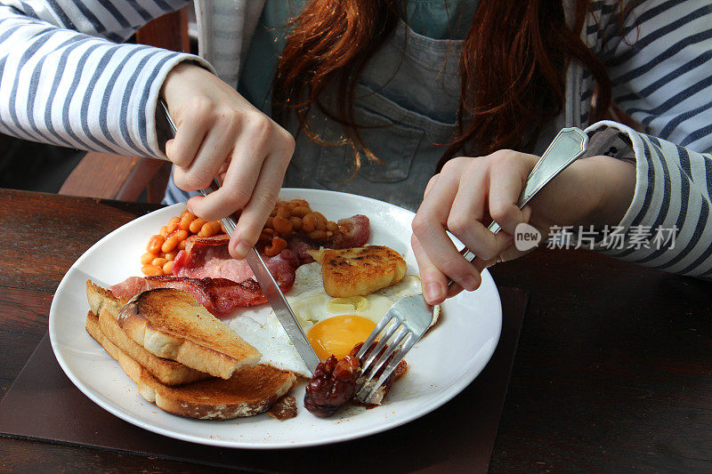 女孩吃饱了英式煎早餐，香肠，鸡蛋，培根，烘豆