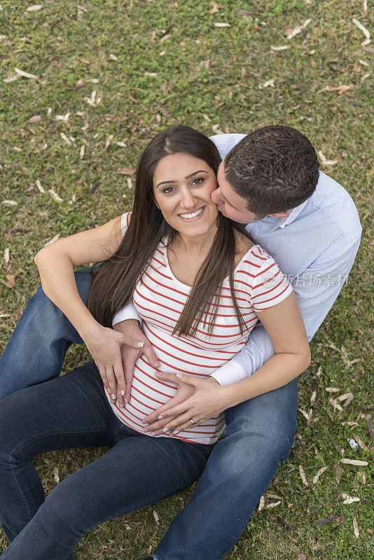 一个男人在公园里亲吻他怀孕的妻子