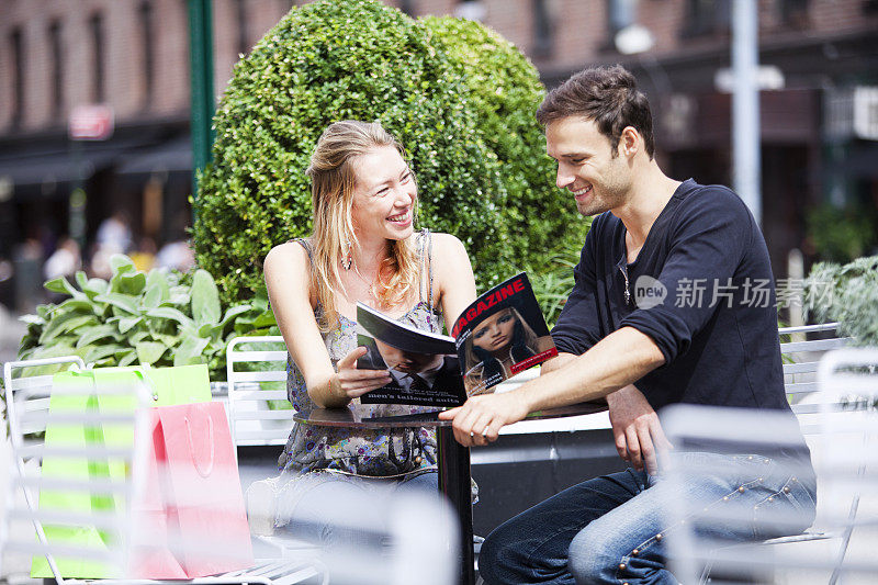 一对年轻幸福的夫妇在户外咖啡馆看杂志