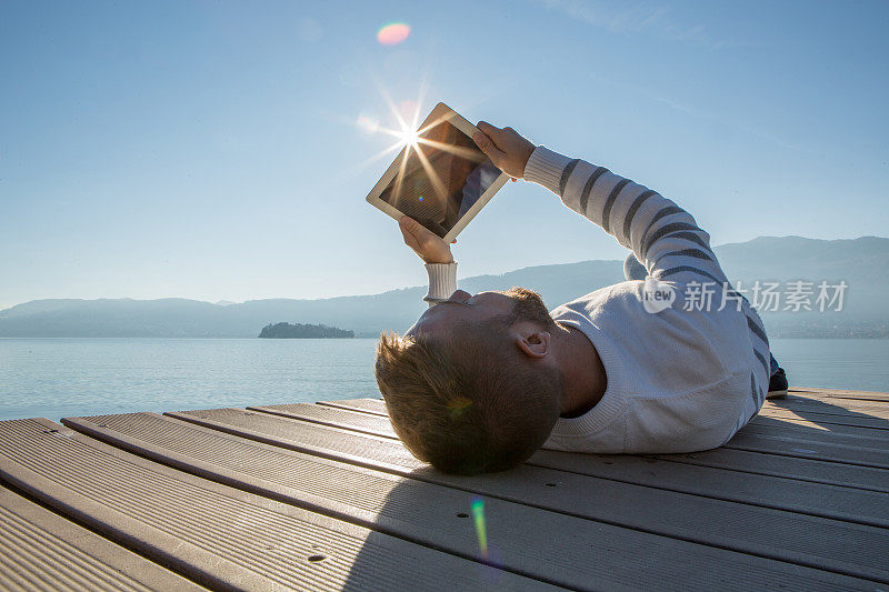 一个年轻人在湖边的码头上玩着平板电脑