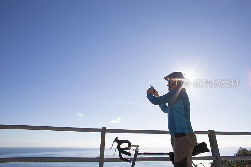 男自行车手用智能手机拍照从公路，到海上