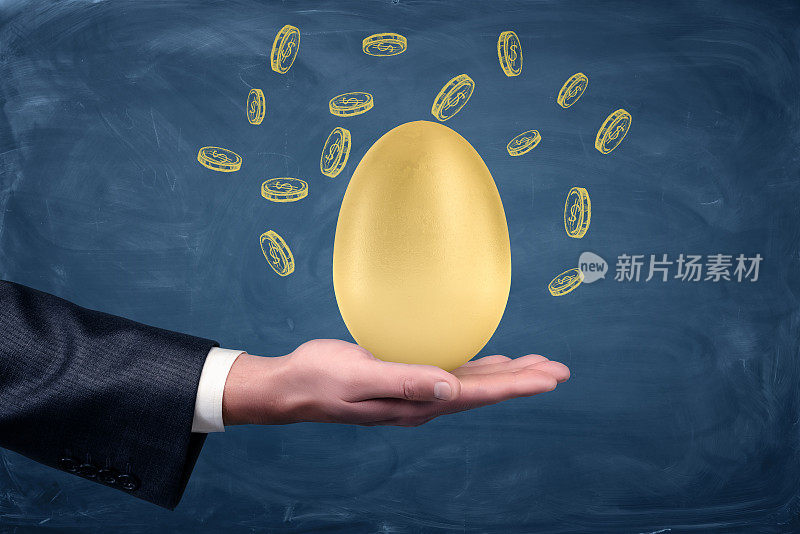 一个商人的手拿着一个大的金蛋在一个蓝色的黑板背景与绘制的美元硬币。
