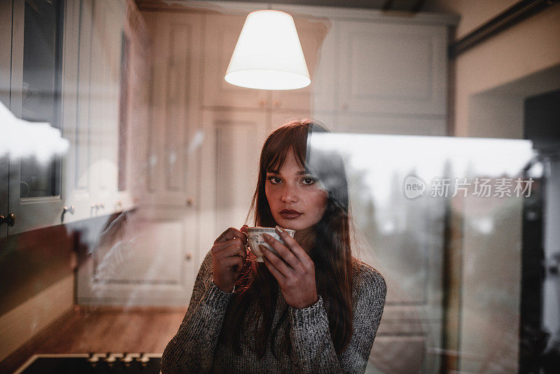 可爱的女性在厨房喝咖啡和看窗外