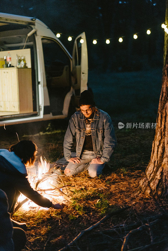 朋友们坐在森林里靠近露营车的篝火旁