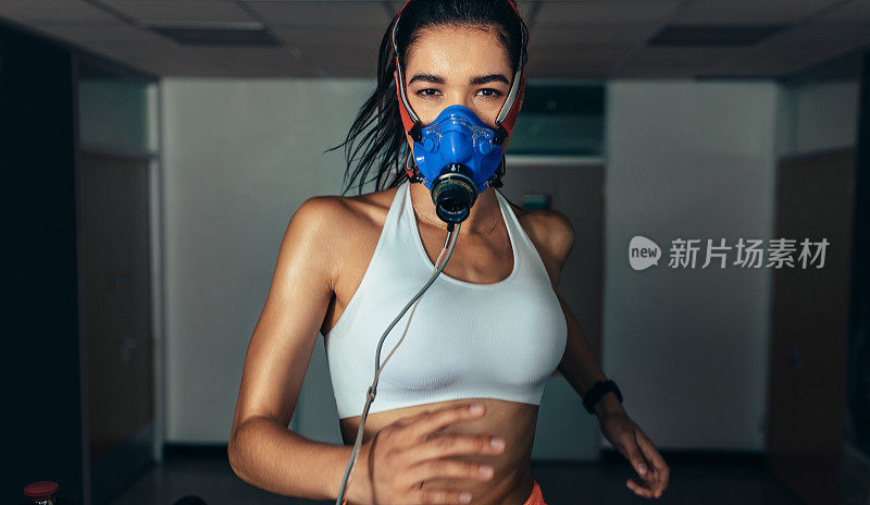 戴着面具在健身房跑步机上跑步的女运动员