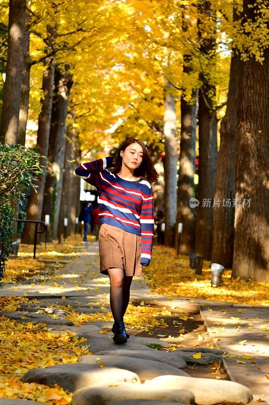 年轻的日本女人享受金黄的银杏树