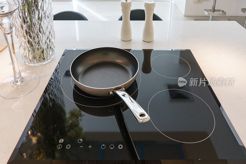 煎锅上的现代黑色电磁炉，炊具，铁架或内置在陶瓷顶部的白色厨房内部