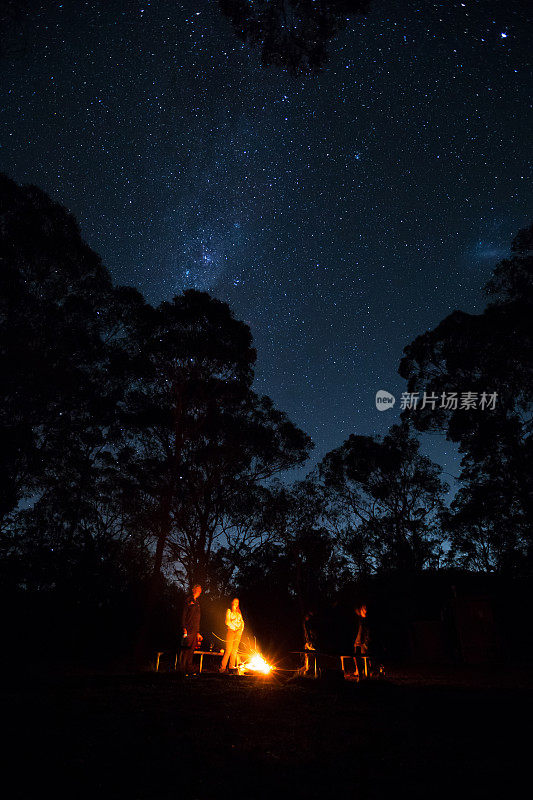 一群露营者围着篝火站着，上面闪烁着明亮的星星