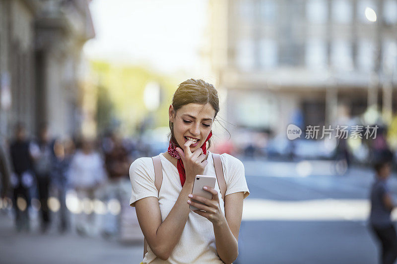 一名年轻女子正带着她的智能手机走在城市的路上