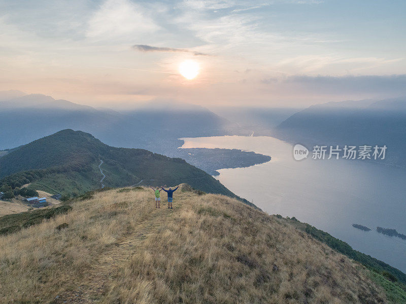 无人机航拍父亲和女儿在清晨徒步登山，拥抱大自然的清新，张开双臂等待成功