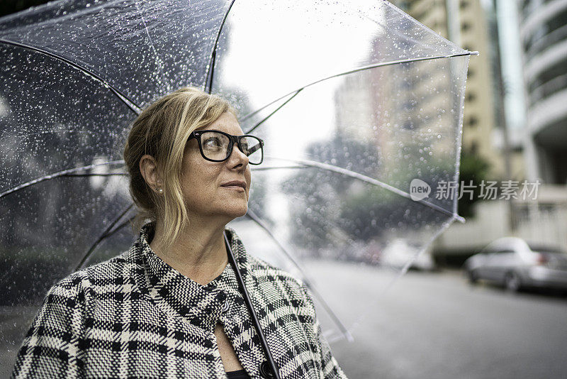 成熟的女人在户外用雨伞看向别处