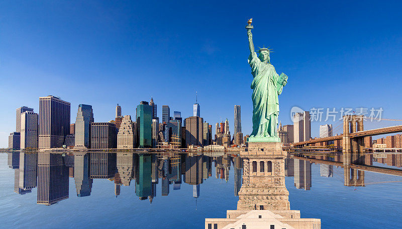 自由女神像和纽约城市天际线与曼哈顿金融区，布鲁克林大桥和世贸中心反映在水中，纽约，美国。