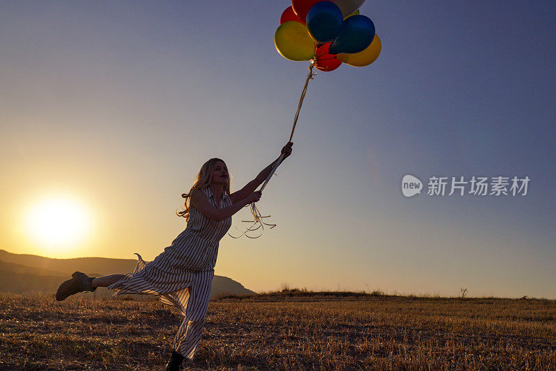 快乐快乐的女孩与气球在夏季日落草地上奔跑