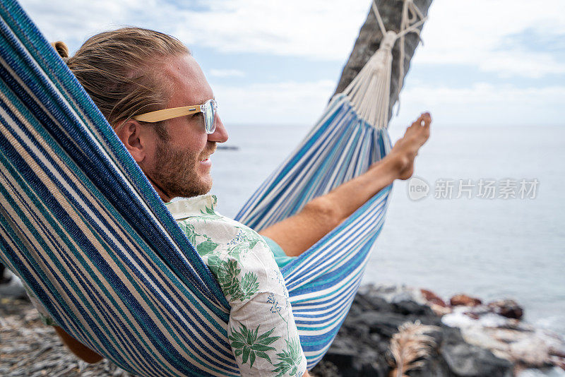 一名男子躺在挂在海滩棕榈树上的吊床上休息