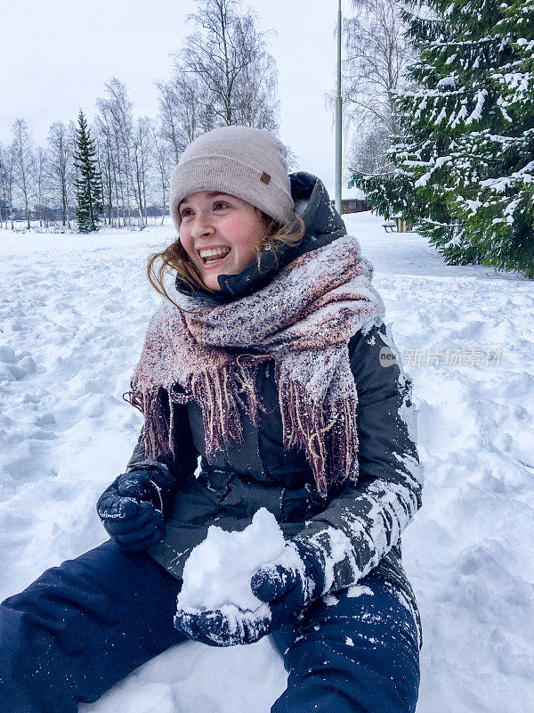 快乐的年轻女子坐在雪中准备雪球