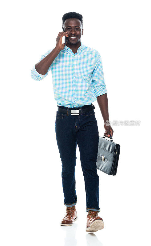 非裔美国青年男性走在白色背景前，穿着智能休闲，拿着公文包，使用智能手机