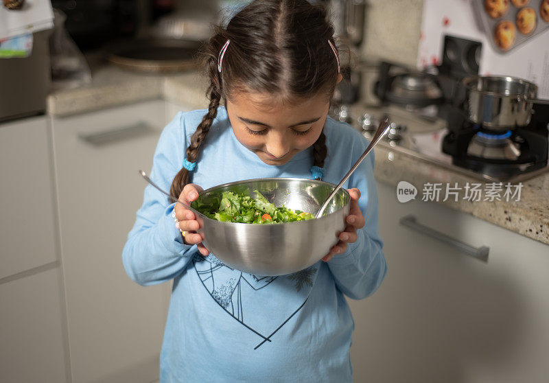 孩子在家做饭。帮助母亲。漂亮的小女孩把沙拉端上了桌子。闻沙拉